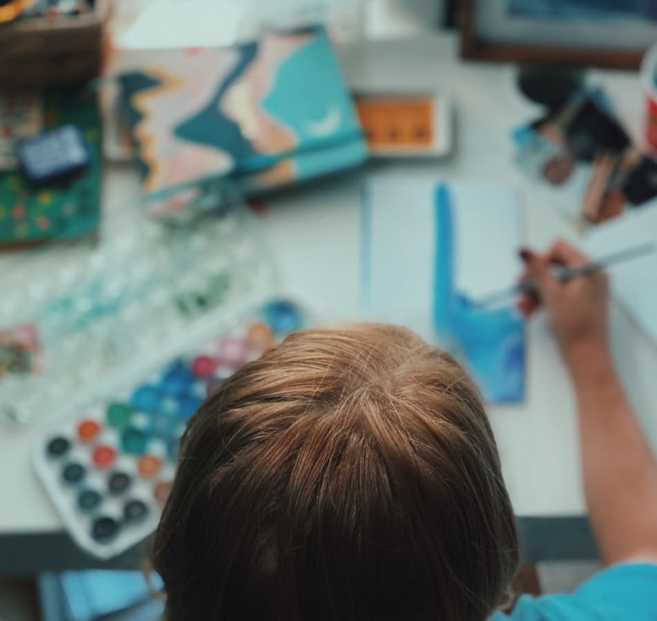 Overhead perspective of an artist painting with watercolor, the background is blurred