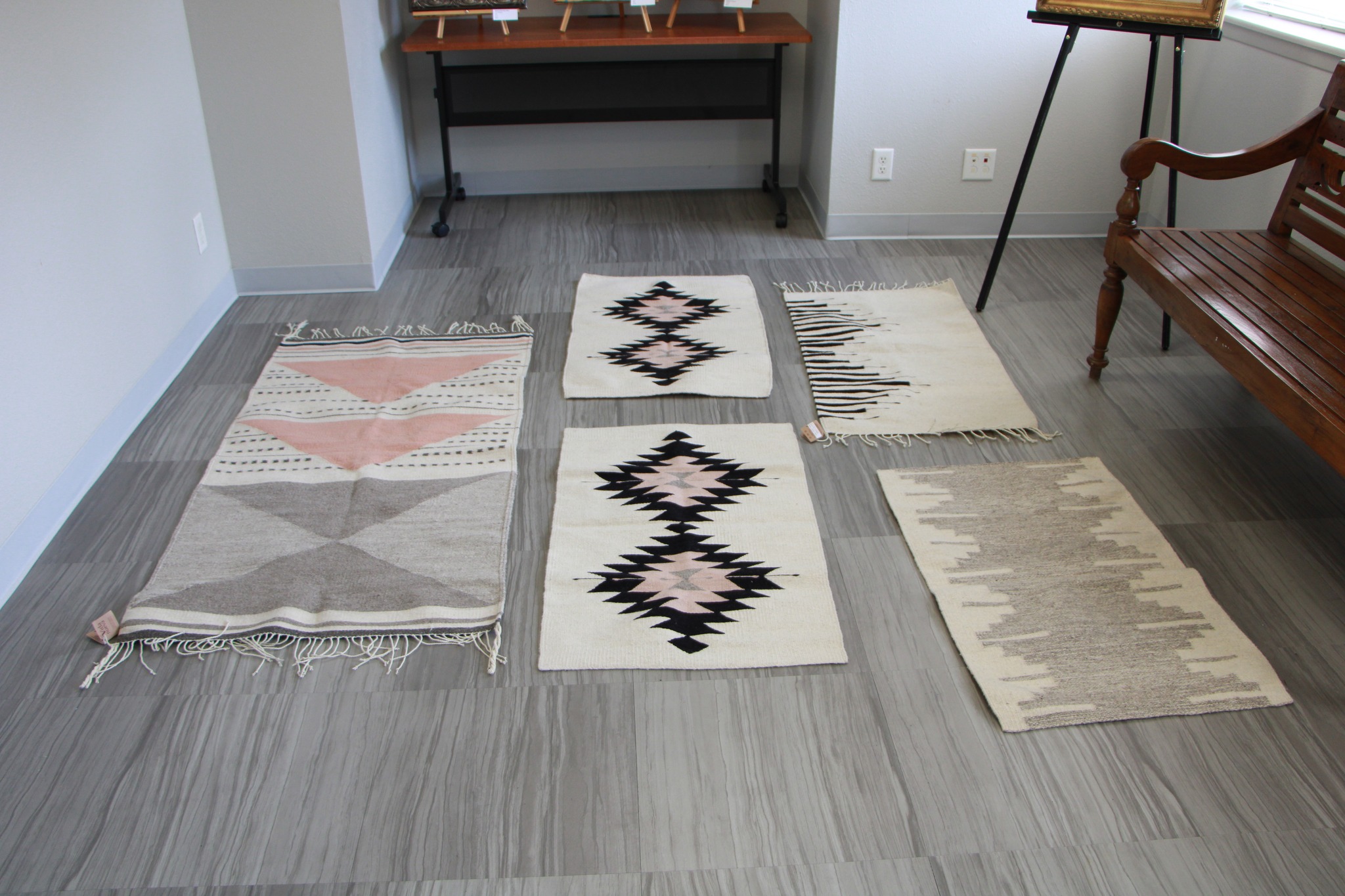 5 handmade, woven rugs lay arranged on the floor, all with various indigenous patterns.