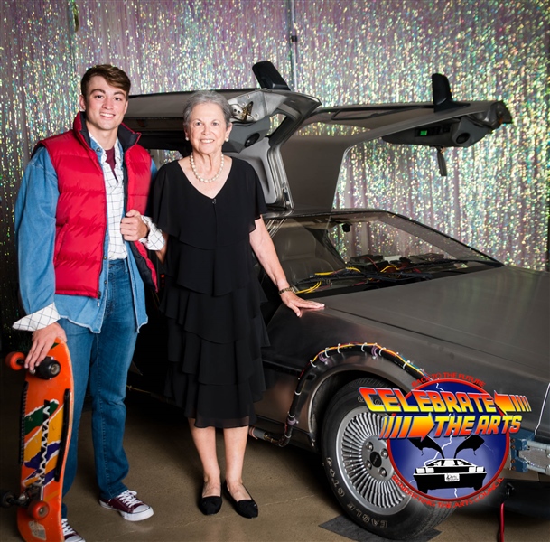 A man dressed as Marty McFly from Back To The Future poses with an older woman in a black dress by the DeLorean time machine.