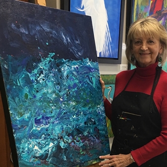 Photo of Coleen Bradfield standing in front of a blue, abstract, acrylic painting.