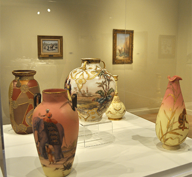 Five ornately painted and gilded vases displayed in a glass case.
