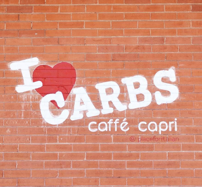 Brick wall with ' I heart carbs - Caffe Capri' painted messily in white letters