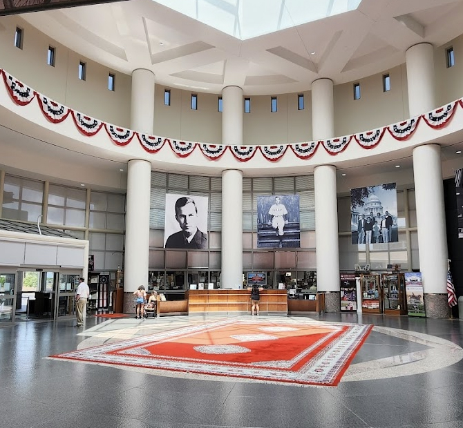 Large, round room with high ceilings. There is a red rug on the ground and a reception desk in the background. Giant posters of George Bush and his family hang on the walls.