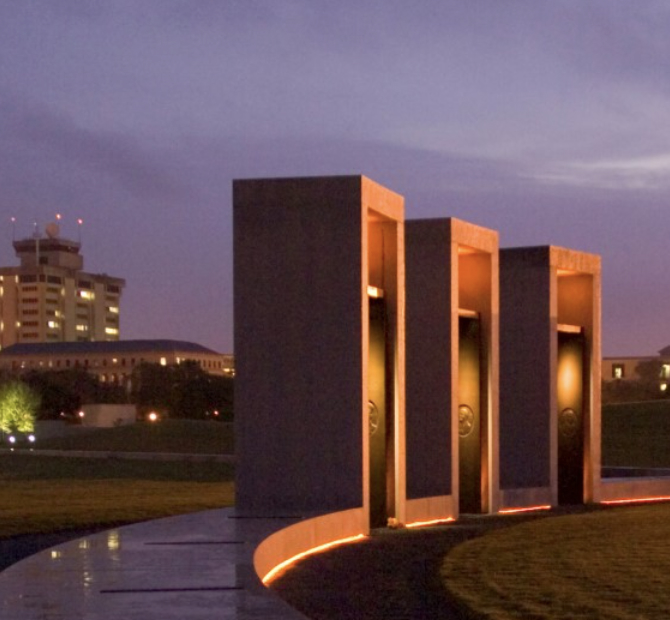 Three monolith sculptures illuminated by soft yellow lights at dusk