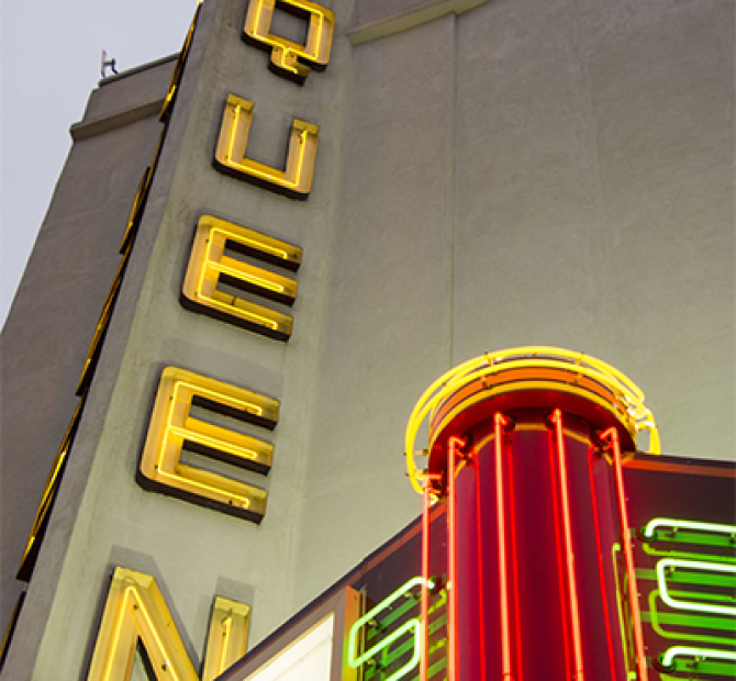 Close up view of a yellow neon movie theater sign that reads 'Queen'