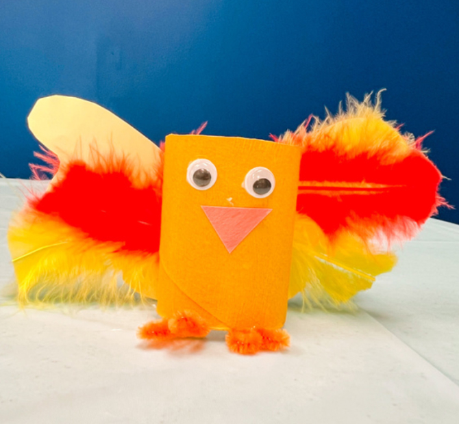 Toilet paper roll bird with orange and yellow feathers, pipe cleaner feet and googly eyes.