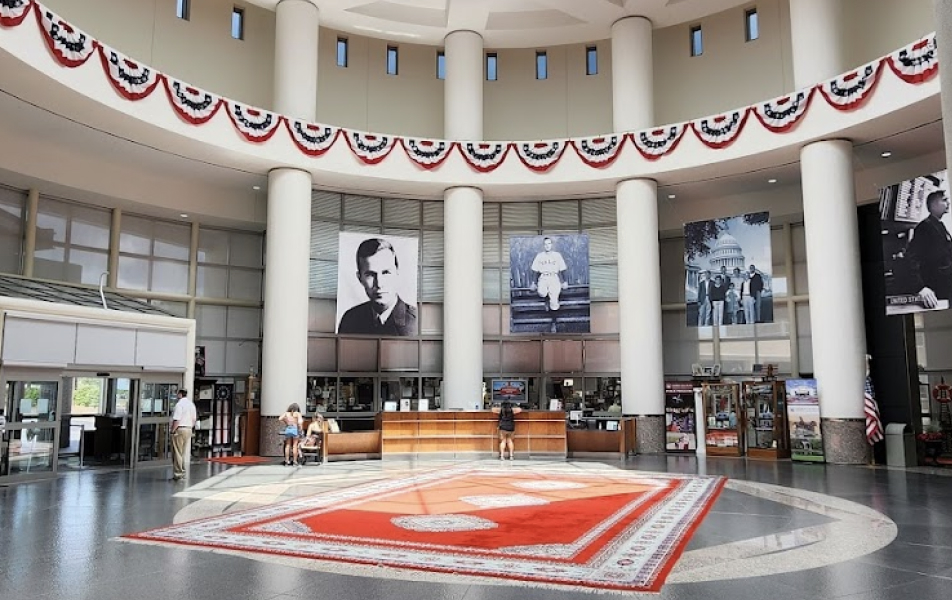 Large, round room with high ceilings. There is a red rug on the ground and a reception desk in the background. Giant posters of George Bush and his family hang on the walls.