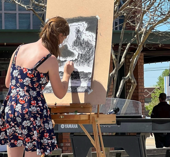 Girl in floral dress draws with charcoals on an easel outside