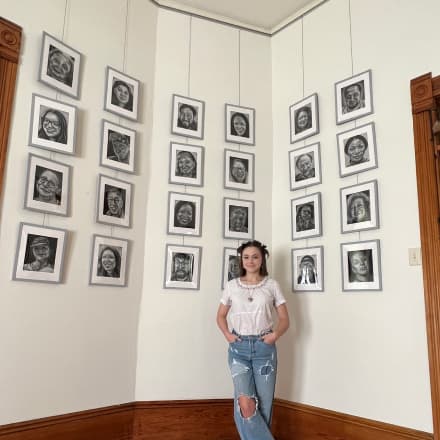 Sara Nevius stands in front of a gallery wall of her black and white portrait illustrations